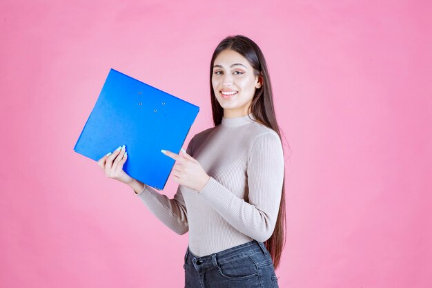 Chica sosteniendo una carpeta de proyecto azul y parece exitosa y feliz