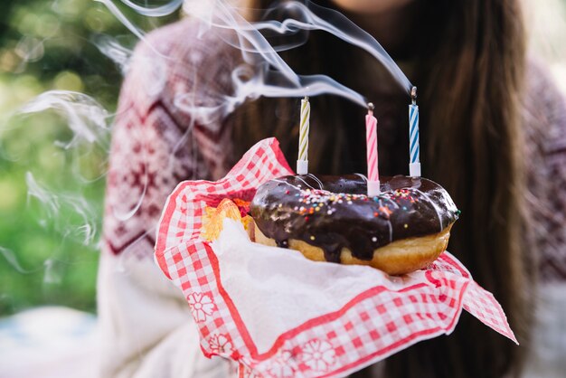 Chica sosteniendo chocolate donut con velas de extinción