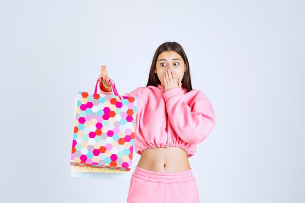 Chica sosteniendo coloridos bolsos de compras y parece sorprendida.