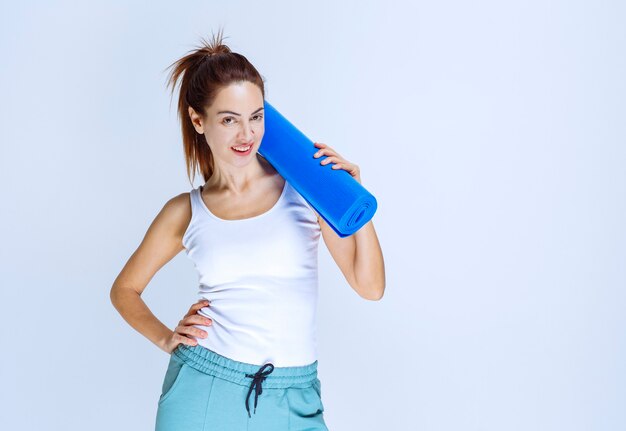 Chica sosteniendo un desenfoque enrollado mate de yoga.