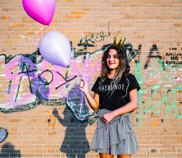 Chica sosteniendo globos delante de muro de grafiti