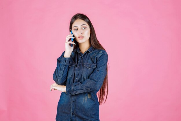 Chica sosteniendo hablando con su teléfono inteligente azul