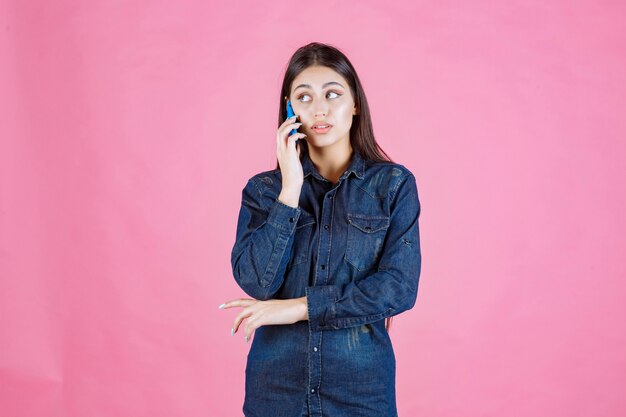 Chica sosteniendo hablando con su teléfono inteligente azul