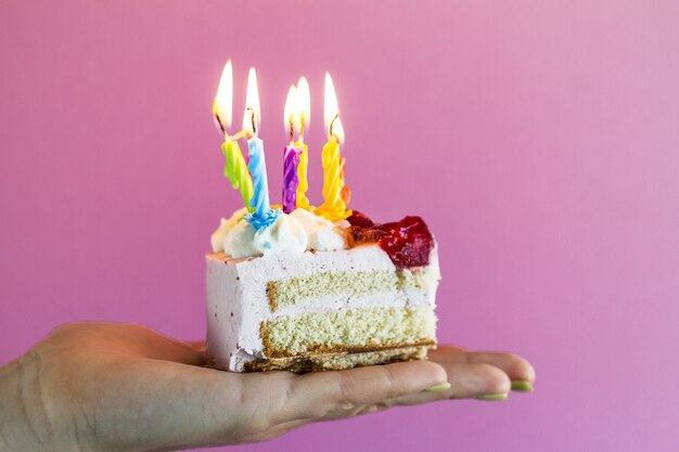 Chica sosteniendo hermosos apetitosos pastel de cumpleaños con muchas velas. De cerca.