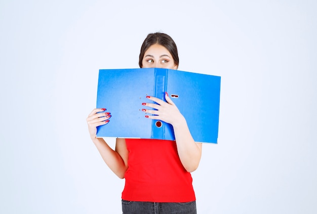 Foto gratuita chica sosteniendo y leyendo una carpeta azul.