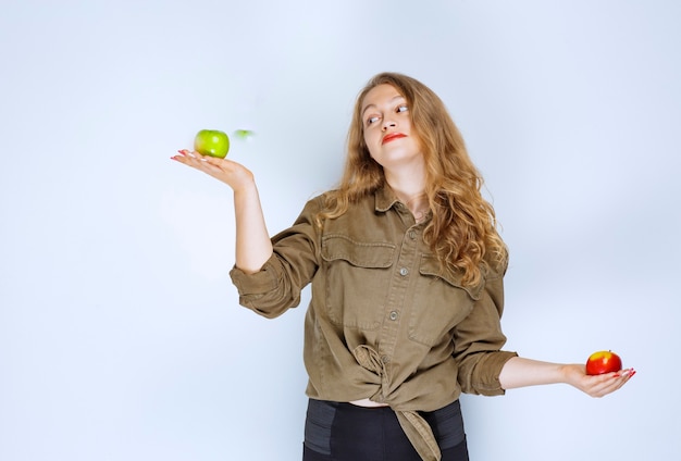 Chica sosteniendo manzanas rojas y verdes en ambas manos.