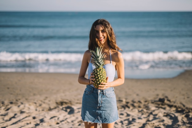 Chica sosteniendo piña por la playa