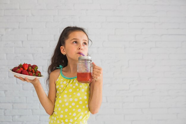 Chica sosteniendo un plato de fresas rojas bebiendo batidos de fresa