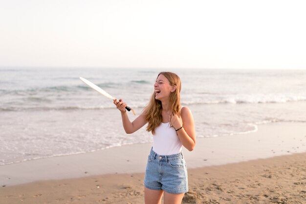 Chica sosteniendo la raqueta de tenis riendo en la playa