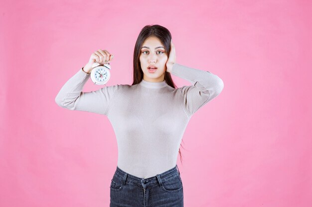 Chica sosteniendo un reloj despertador y tapándose la oreja debido al alto volumen