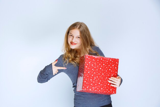 Chica sosteniendo su caja de regalo roja y mostrándola.