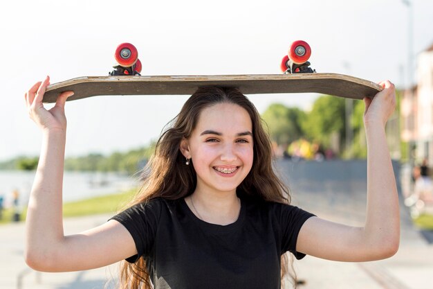 Chica sosteniendo su patineta sobre su cabeza afuera