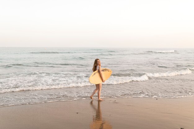 Chica sosteniendo la tabla de surf de pie cerca de la orilla del mar