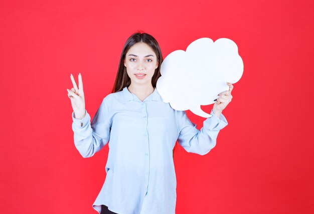 Chica sosteniendo un tablero de información de forma de nube y mostrando un signo de mano positivo.