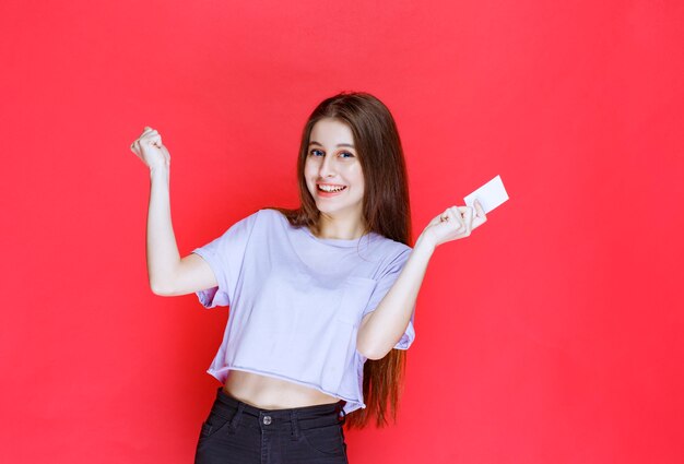 Chica sosteniendo una tarjeta de visita y mostrando un signo de mano positivo.
