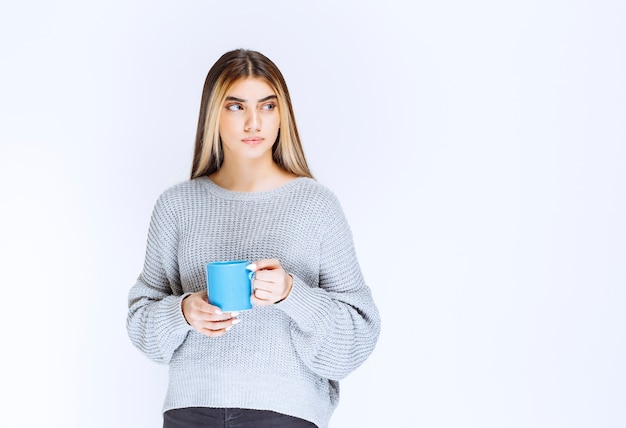 Chica sosteniendo una taza de café azul y promocionándola.
