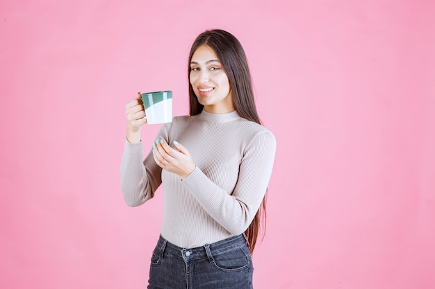 Chica sosteniendo una taza de café de color verde blanco y sintiéndose positivo