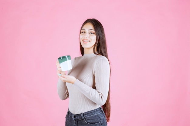 Chica sosteniendo una taza de café de color verde blanco y sintiéndose positivo