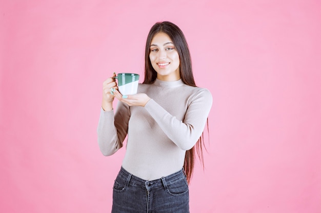 Chica sosteniendo una taza de café de color verde blanco y sintiéndose positivo