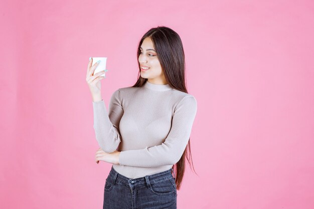 Chica sosteniendo una taza de café desechable blanca, promocionándola u oliendo el café recién hecho