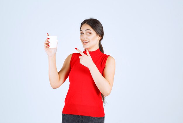 Chica sosteniendo una taza de café con leche y apuntando a ella.