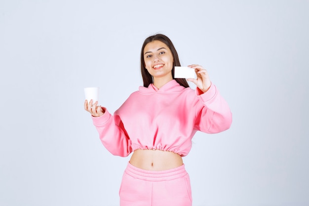 Chica sosteniendo una taza de café en una mano y presentando su tarjeta de visita en la otra mano