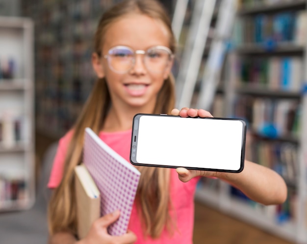 Chica sosteniendo un teléfono de pantalla vacía en la biblioteca