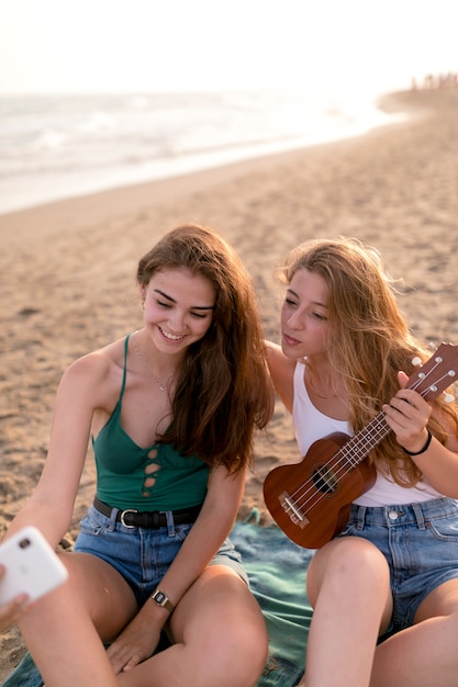 Chica sosteniendo ukelele tomando selfie con su amigo en la playa