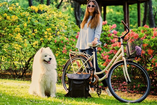 Una chica con su perro y una bicicleta al fondo de un parque.