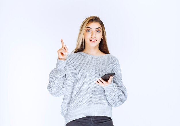 Chica en sudadera gris sosteniendo un teléfono inteligente negro y tiene una buena idea.