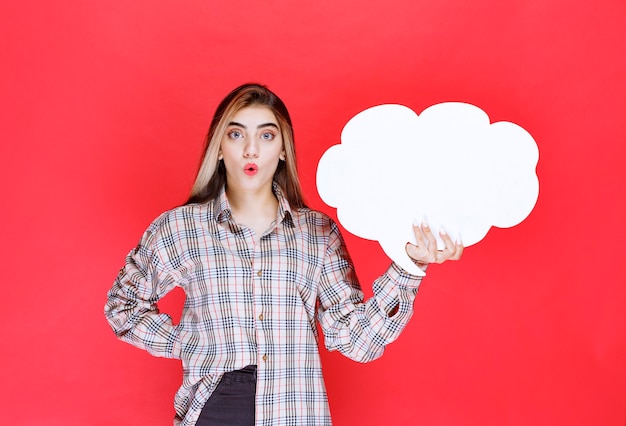 Chica en suéter cálido sosteniendo un tablero de ideas con forma de nube y parece sorprendida