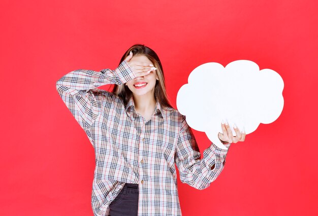 Chica en suéter cálido sosteniendo un tablero de ideas con forma de nube y se siente cansada debido a esta actividad