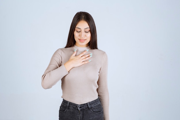 Chica de suéter gris apuntando a sí misma.