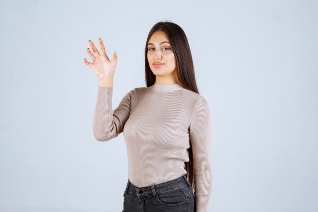 Chica en suéter gris haciendo signo de lobo.