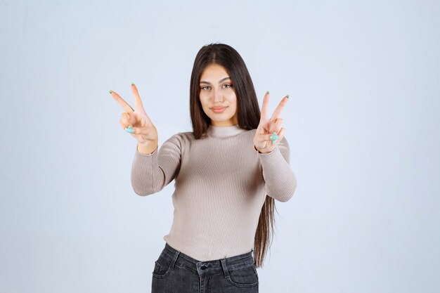 Chica en suéter gris haciendo el signo de la mano de la paz.