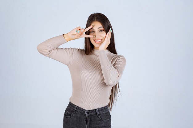 Chica en suéter gris haciendo el signo de la mano de la paz.