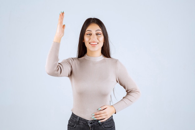 Chica de suéter gris levantando las manos.
