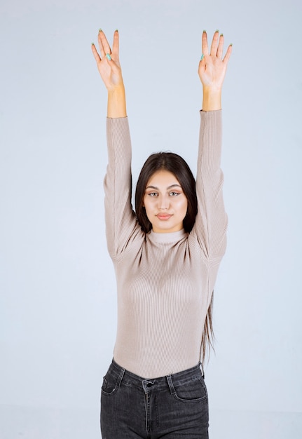 Chica de suéter gris levantando las manos.