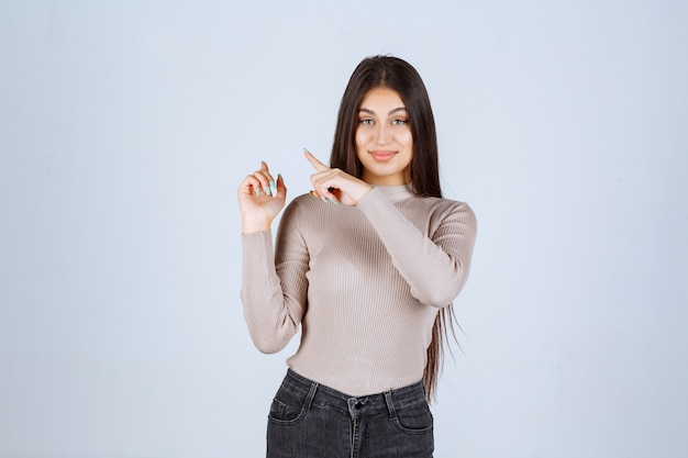 Chica en suéter gris mostrando algo a la izquierda.