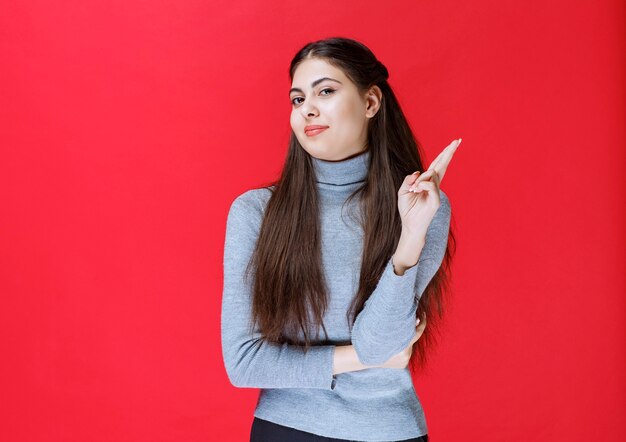 Chica en suéter gris que muestra el signo de la cruz del dedo.