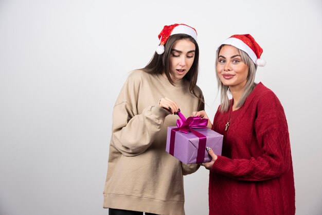 Chica de suéter rojo dando un regalo a la chica de suéter beige.