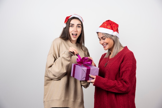 Chica de suéter rojo dando un regalo a la chica de suéter beige.