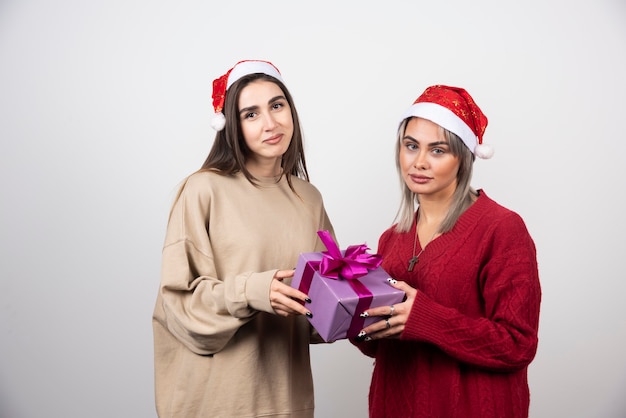 Chica de suéter rojo dando un regalo a la chica de suéter beige.