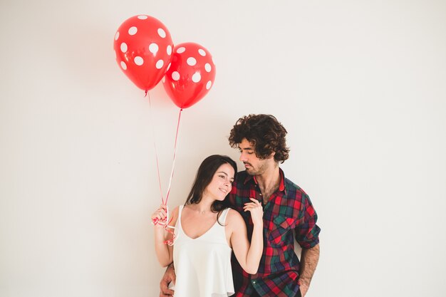 Chica sujetando dos globos mientras apoya la cabeza en el pecho de su novio