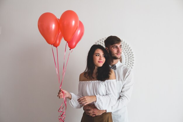 Chica sujetando globos con forma de corazón mientras su novio la abraza