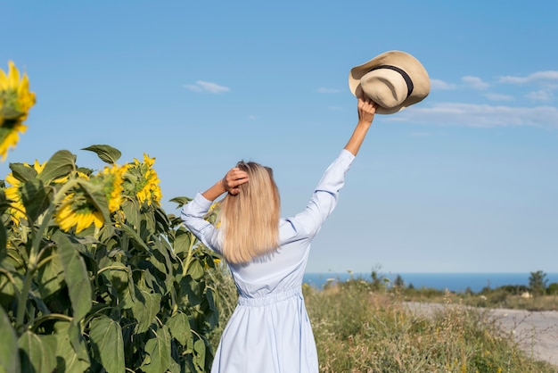 Chica sujetando su sombrero en un campo con flores de sol