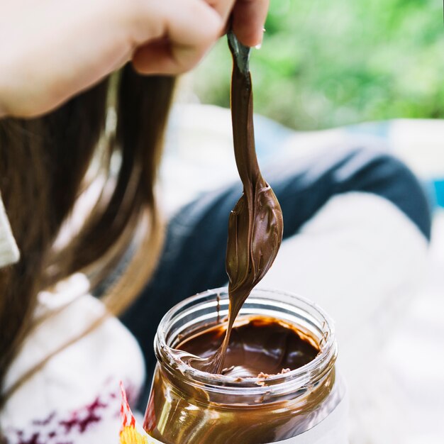 Chica sumergir la cuchara en el tarro de chocolate derretido