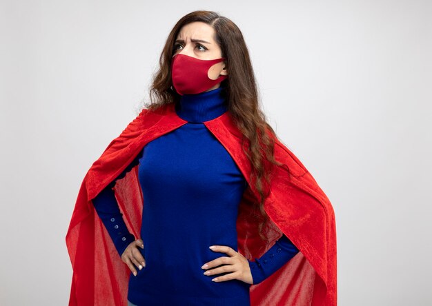 Chica superhéroe caucásica disgustada con capa roja con máscara protectora roja
