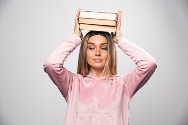 Chica en swaetshirt rosa sosteniendo sus libros sobre su cabeza