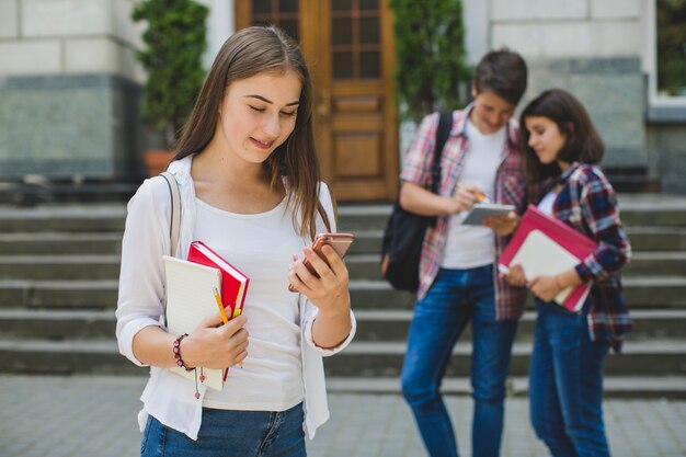 Chica con teléfono y compañeros de clase en la calle